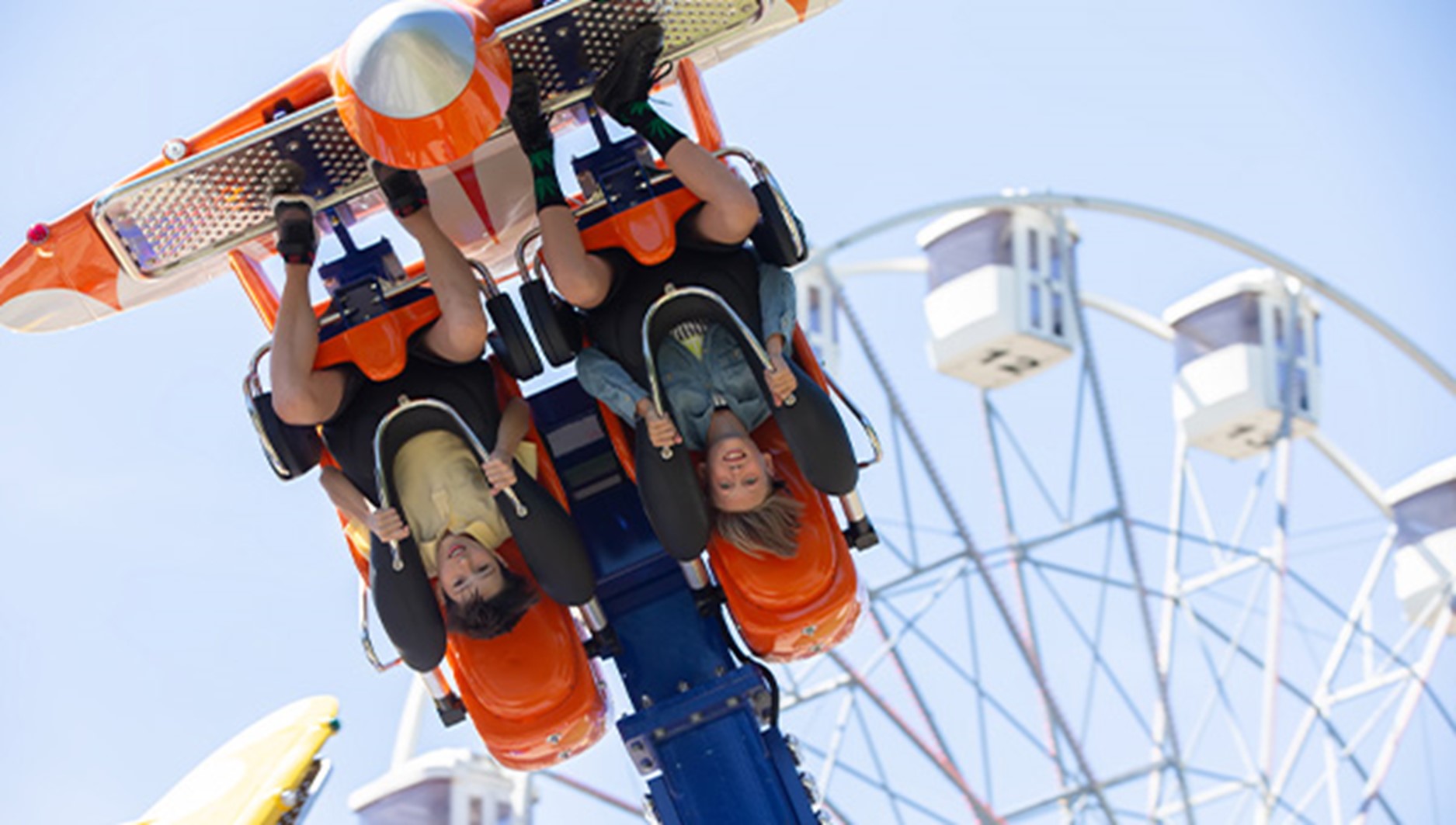 Two kids hang upside down on a roller coaster ride.