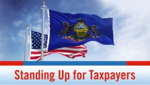 The Pennsylvania and American flags fly in front of a partly cloudy sky.