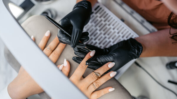 Mid-adult woman getting her French nails drawn on by a female nail technician at the beauty salon. Close-up.