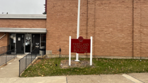 A red sign reading “Freeland Borough Building” outside a brick building.