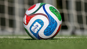 A soccer ball with FIFA World Cup branding sits on a grassy field.